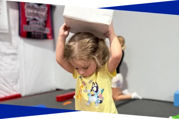 Toddler carrying a soft block during a parent assisted tumbling class at Genesis Athletix