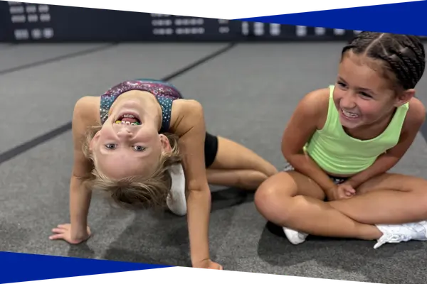 Two young tumbling students smiling during a bridge drill at Genesis Athletix