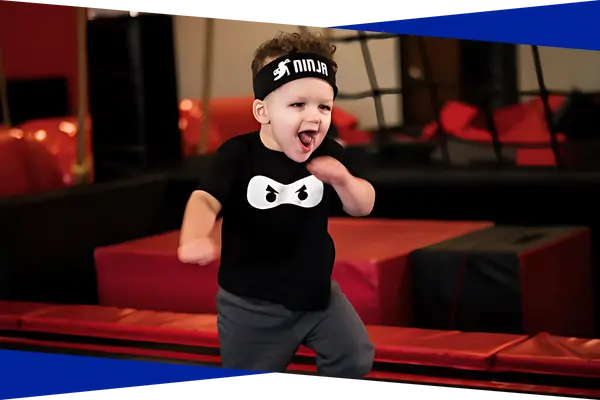 Toddler in a ninja headband running through a padded obstacle course at Genesis Athletix