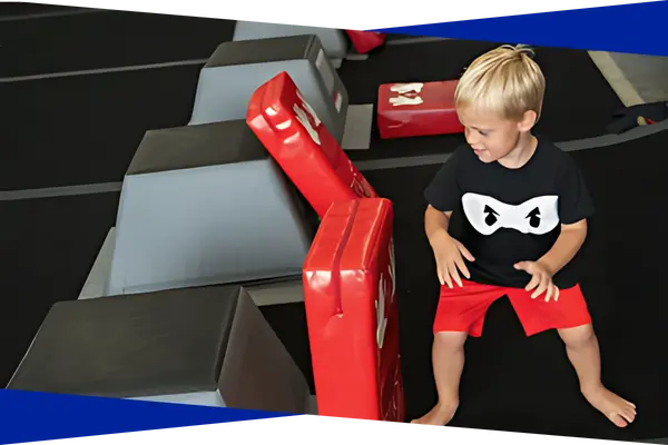 Preschool aged ninja student climbing over red and gray obstacle blocks